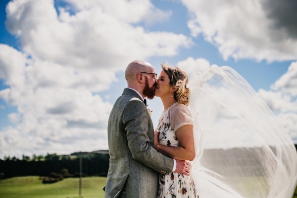 Bride and groom kiss sky in background embracing