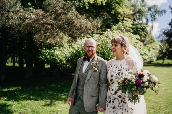 Bride and groom walk on grass together hand in hand