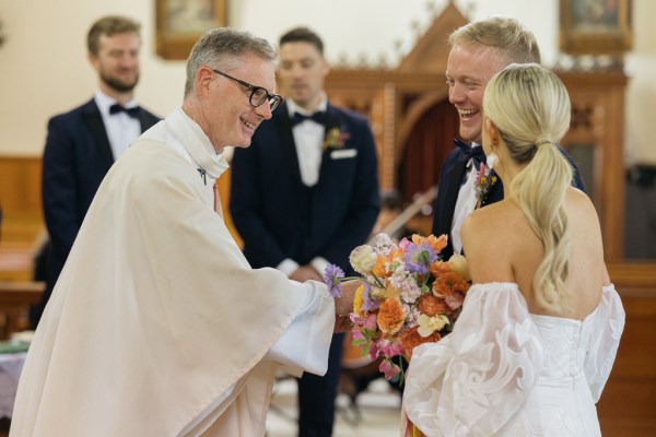 Priest bride and groom smile laughing