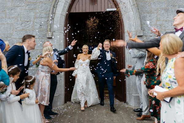 Confetti being thrown on bride and groom guests outside church setting couple smiling celebrating they exit church