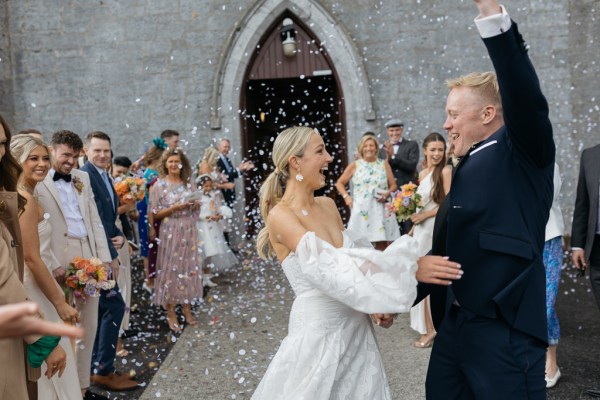 Confetti being thrown on bride and groom guests outside church setting couple smiling celebrating