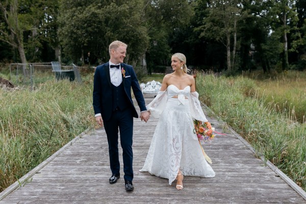 Bride and groom walk along boardwalk hand in hand together