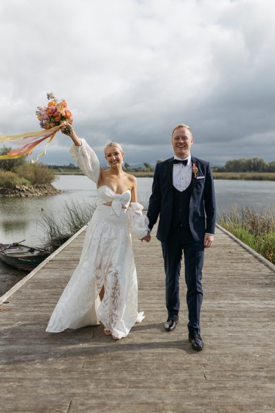 Bouquet in the air holding hands with groom bride smiles lake in background