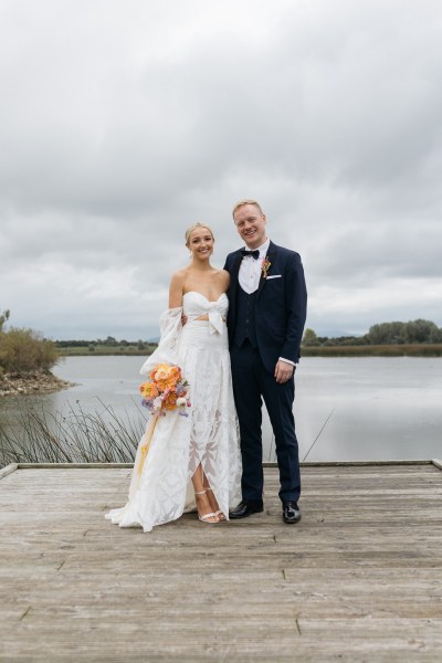 Bride and groom laugh on the boardwalk bouquet in shot lake in background