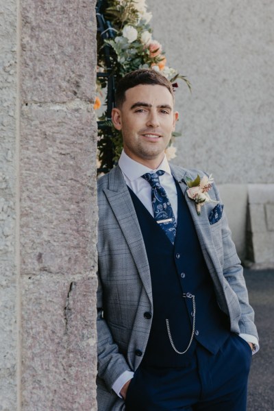 Groom leans against wall and poses for camera in suit