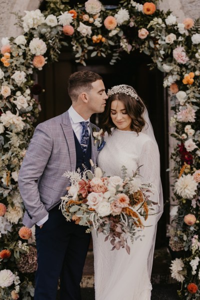 Groom kisses bride on the head as she holds bouquet of flowers