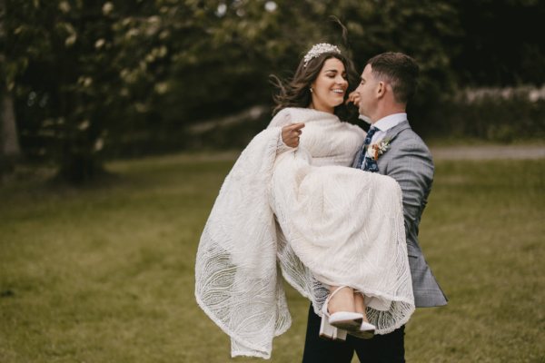 Groom picks up bride on grass they smile together