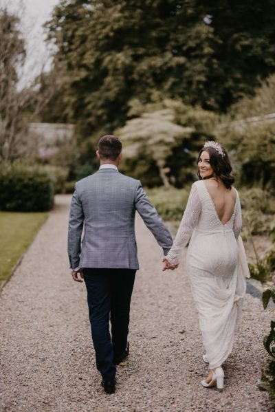 Bride looks over her shoulder at camera holding grooms hand