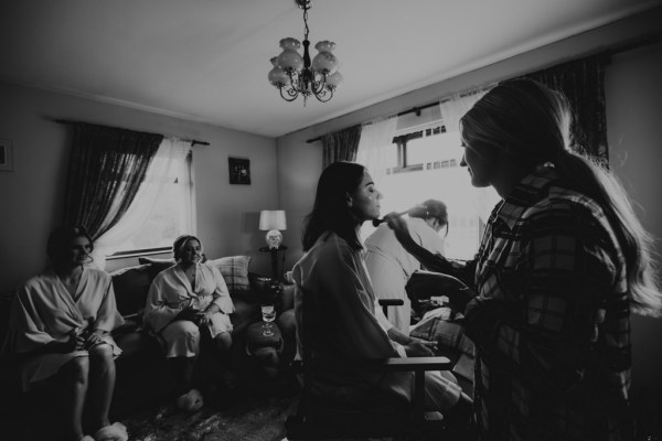 Black and white image of bride and bridesmaids getting makeup done by MUA