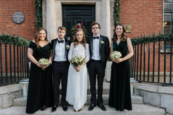 Group shot bride groom bridesmaids and groomsmen pose in front of door