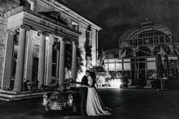 Bride and groom standing beside wedding car outside wedding venue