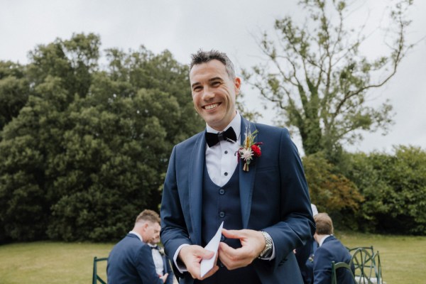 Groom holding card vows outside smiling