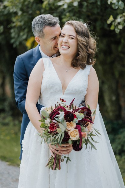 Hug from behind bride and groom smiling bouquet in hands