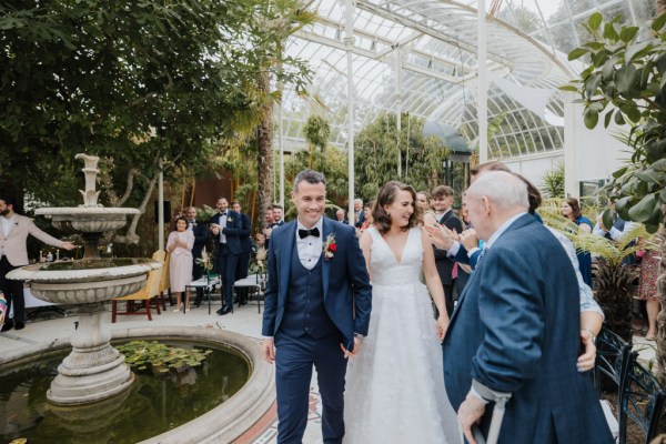 Bride and groom walk along fountain ceremony room with guests