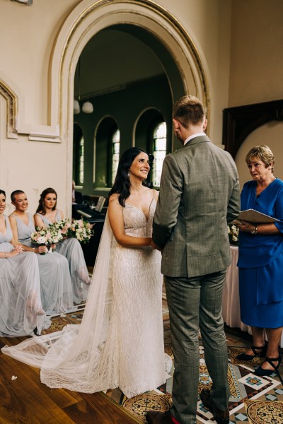 Celebrant bride and groom at alter to church holding hands bridesmaids in background