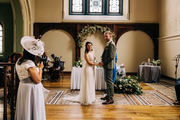 Bride and groom look out at guests/audience as they stand at alter