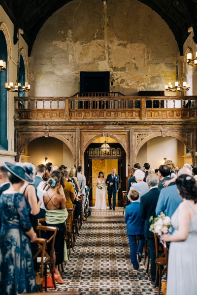 Father of the bride walks bride down the aisle surrounded by guests