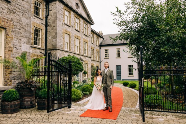 Bride and groom walk in the garden and smile at each other on orange carpet