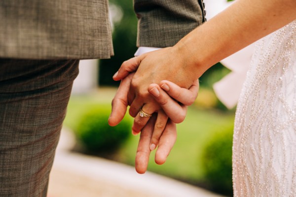 Bride and groom hold hands in the garden close up