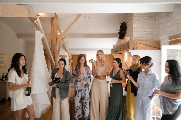 Bride and bridesmaids open bottle of champagne prosecco group photo cheers celebrating