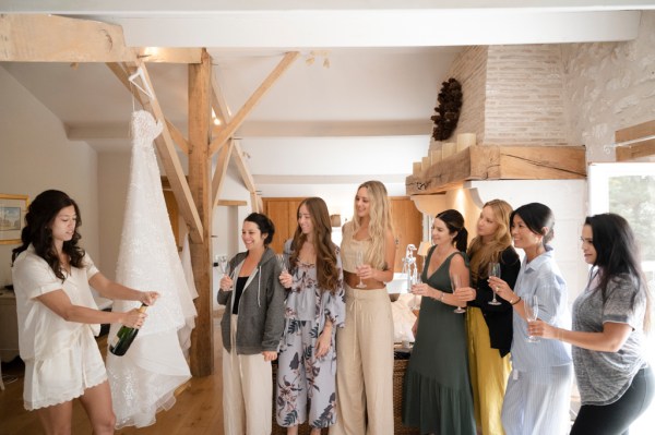 Bride and bridesmaids open bottle of champagne prosecco group photo cheers celebrating