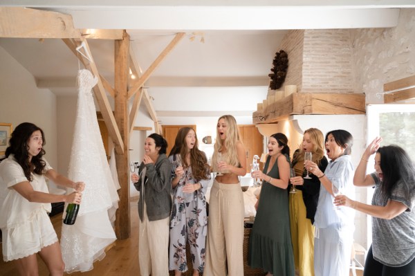 Bride and bridesmaids open bottle of champagne prosecco group photo cheers celebrating