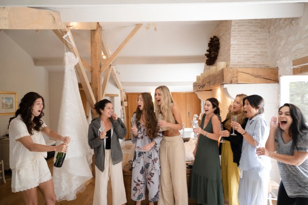 Bride and bridesmaids open bottle of champagne prosecco group photo cheers celebrating