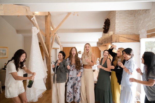 Bride and bridesmaids open bottle of champagne prosecco group photo cheers celebrating