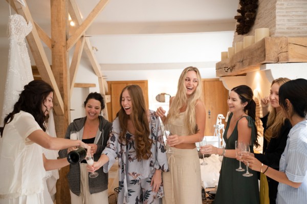 Bride and bridesmaids open bottle of champagne prosecco group photo