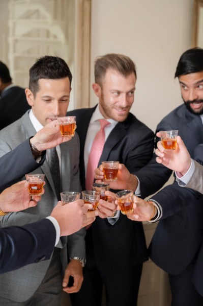 Groom and groomsmen cheers with glass of whiskey