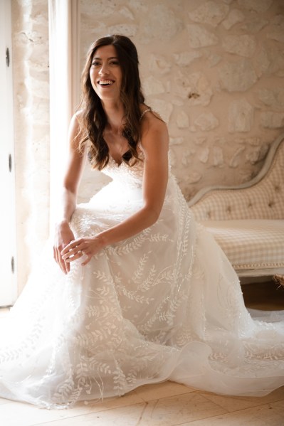 Bride sits and smiles/laughs as she gets ready