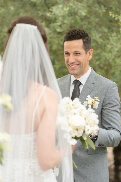 Groom smiles at bride during ceremony veil detail