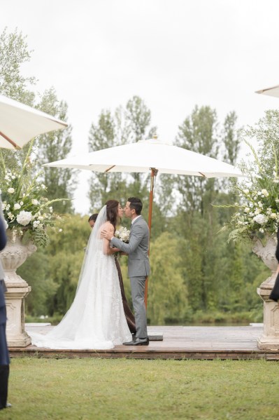 Bride and groom stand under umbrella away from the rain they kiss kissing