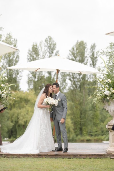 Bride and groom stand under umbrella away from the rain