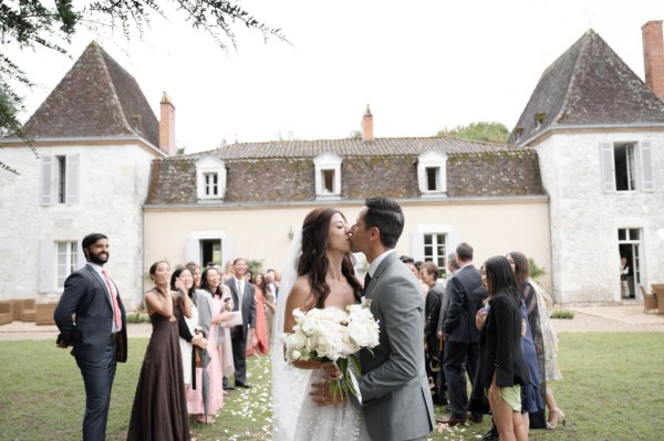 Bride and groom kiss in front of guests holding white bouquet flowers