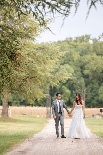 Bride and groom walk hand in hand together along pathway to park