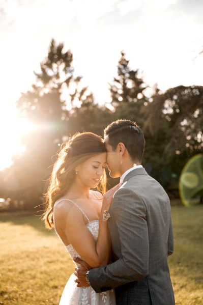 image of bride and groom holding each other sun shining through couple in park trees