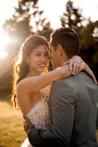 image of bride and groom holding each other sun shining through couple in park trees