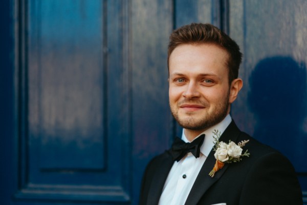 Happy smiling groom stands beside blue-painted door