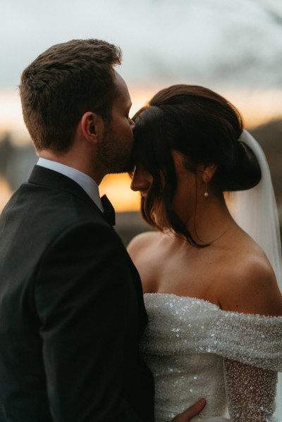 Dark evening shot of bride and groom kiss on the forehead hair