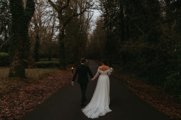 Bride and groom are hand in hand holding hands in dark moody forest