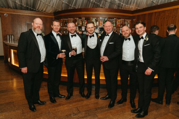 Groom groomsmen friends best man pose inside tent marquee together