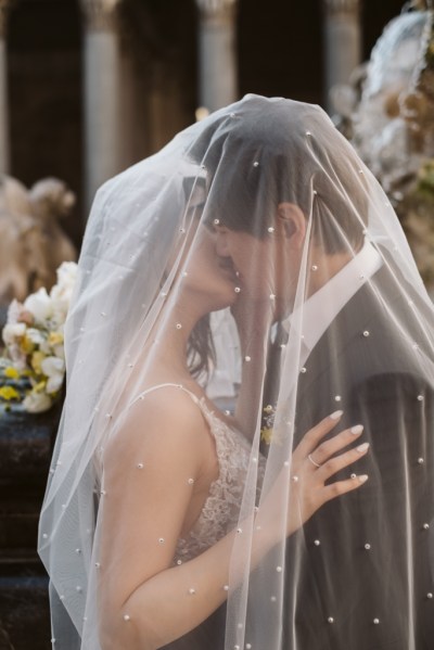 Veil covers both bride and groom as they kiss underneath