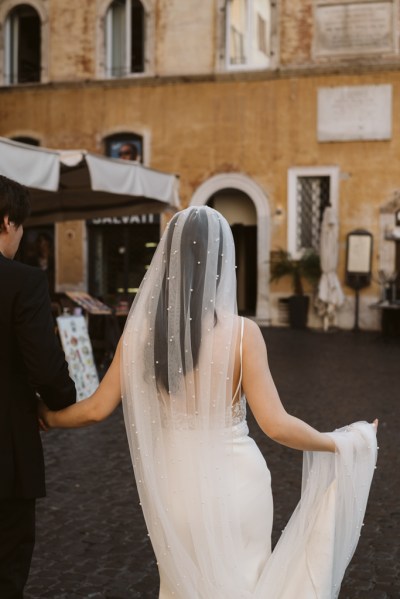 Back of brides veil dress and groom arm in arm