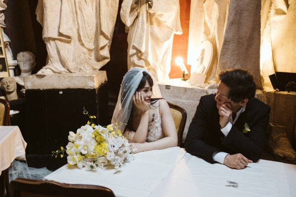 Statues behind couple bride and groom sit and sign marriage cert