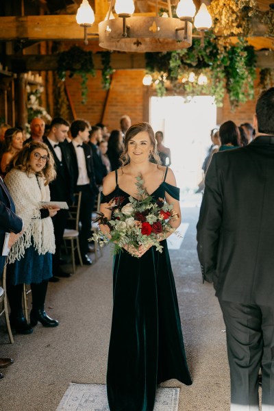 Bridesmaid in black dress holding bouquet walks down the aisle towards alter