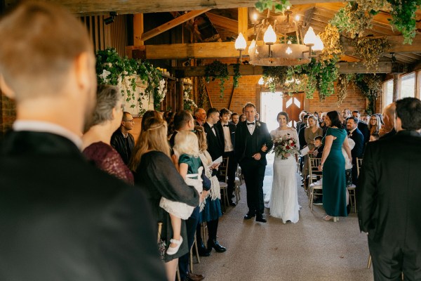 Father of the bride walks down the aisle surrounded by guests groom awaits her