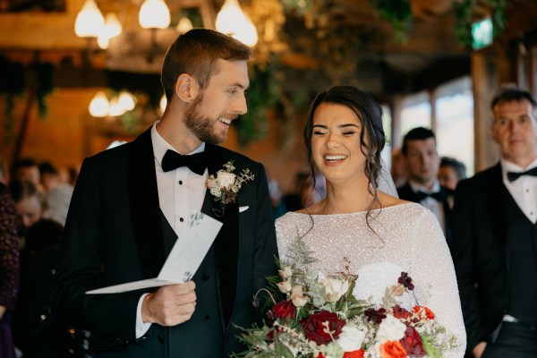 Bride and groom at top of alter reading from booklet in front of guests they laugh laughing