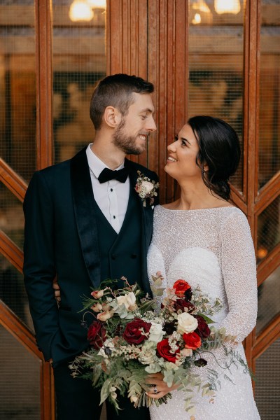 Bride and groom look at each other smiling she holds bouquet