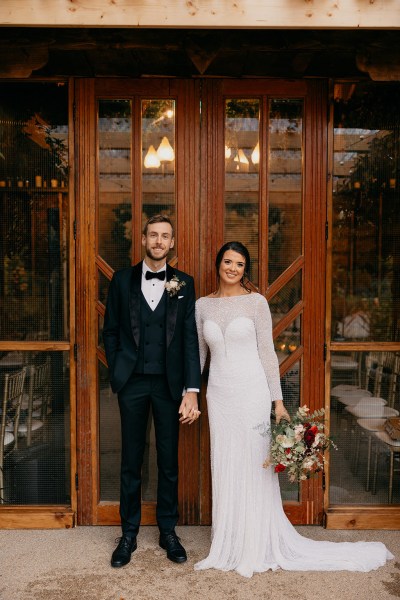 Bride and groom hold hands hand in hand holding bouquet/flowers at wedding venue entrance